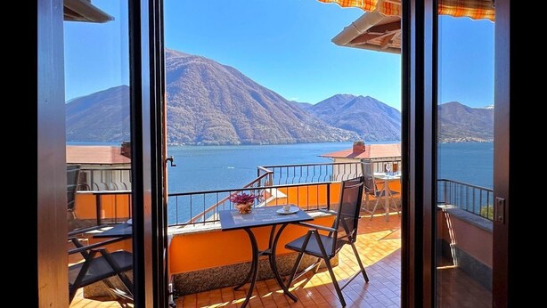 Un balcón con mesa y sillas, con vistas a un lago y montañas.
