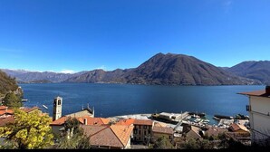 Un pueblo a orillas del lago, con una montaña destacada al fondo, una iglesia con campanario y un puerto deportivo con barcos.