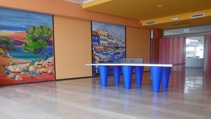 Mesa de pingue-pongue em um espaço com piso de azulejos e duas grandes pinturas nas paredes.