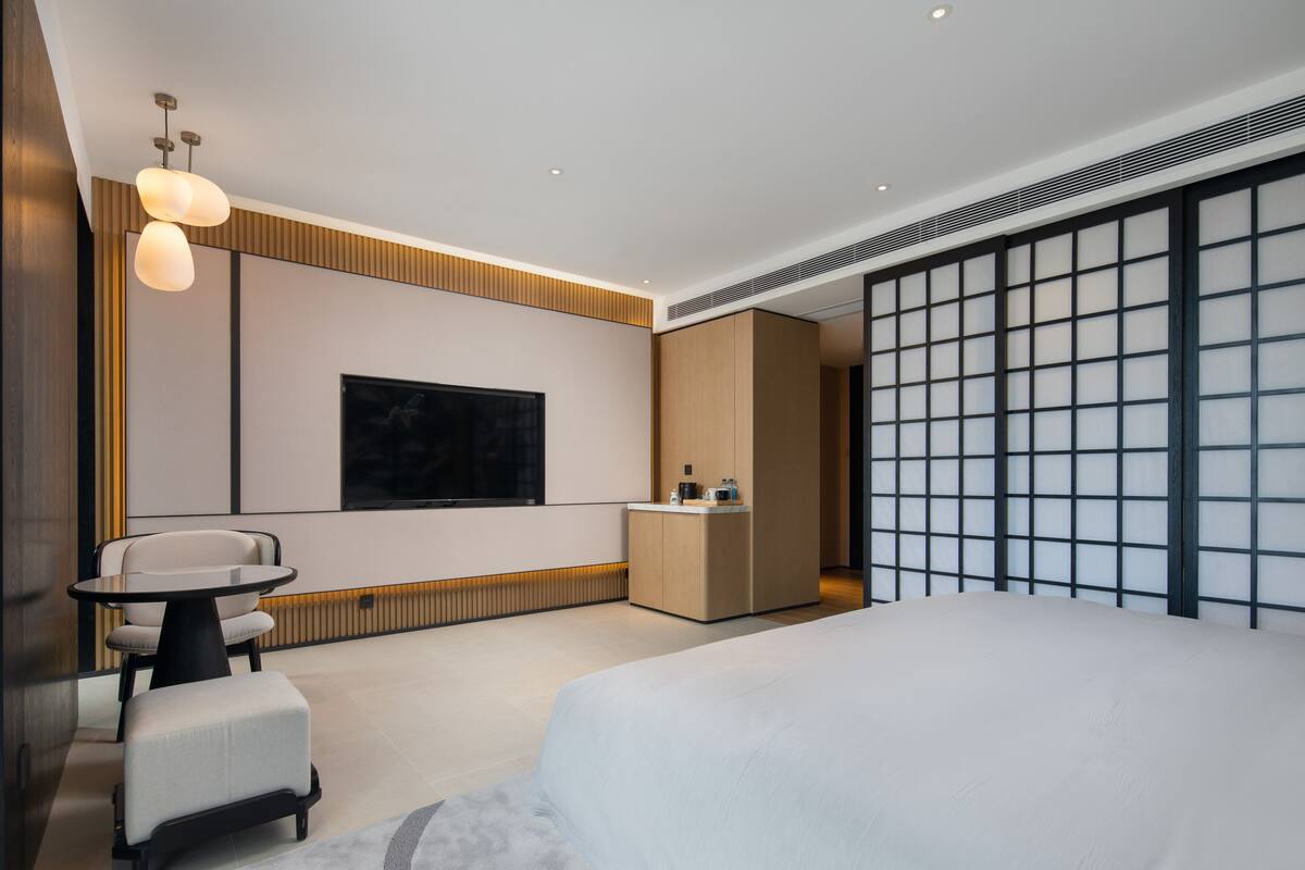 Ein modernes Hotelzimmer mit einem großen Bett, einem kleinen runden Tisch, einer Couch, einem Fernseher und einer Minibar.