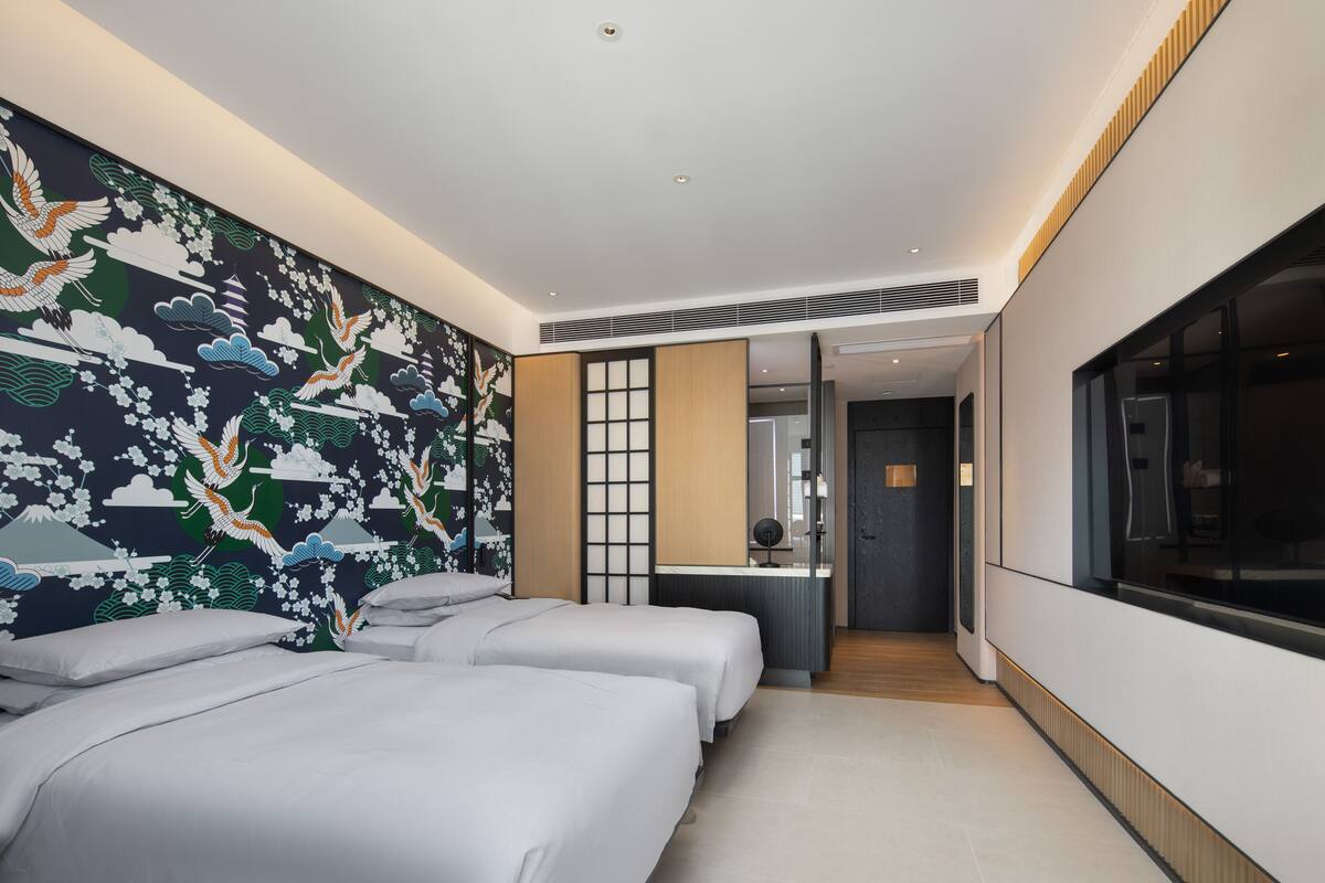 Ein modernes Hotelzimmer mit zwei Betten, einem großen Fenster und einer Wandmalerei im traditionellen japanischen Stil.