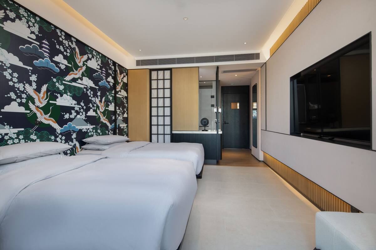 Ein modernes Hotelzimmer mit zwei Betten, einem großen Fernseher und einer Wand mit traditioneller Kunst.