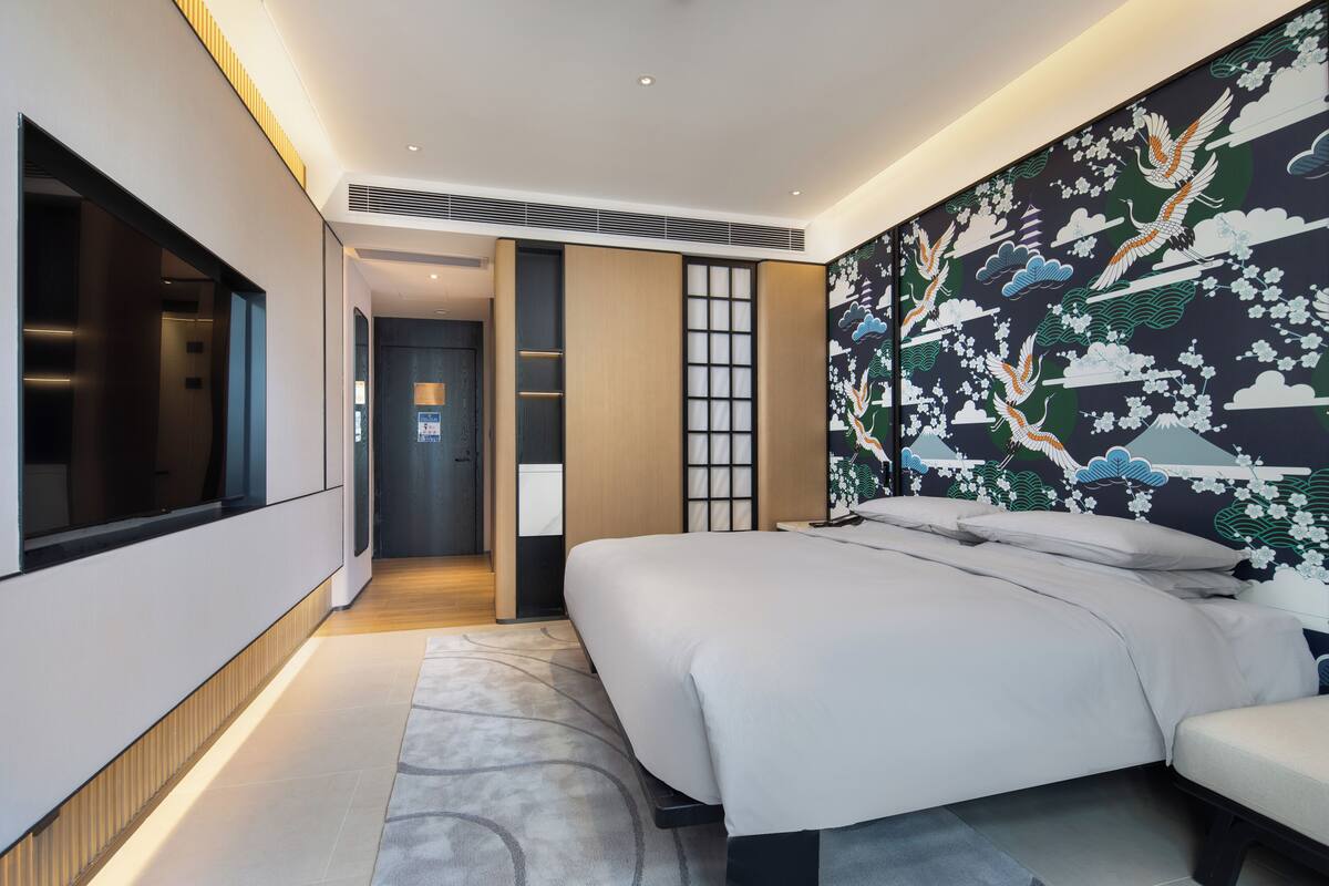 Ein modernes Hotelzimmer mit einem großen Bett, einem Flachbildfernseher und einer traditionellen japanischen Wandmalerei.