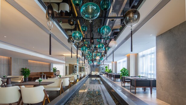 A modern hotel lobby with a central water feature, seating areas, and a ceiling adorned with spherical glass fixtures. - GINCO Hotel Guangzhou Baiyun Airport (Guangzhou)