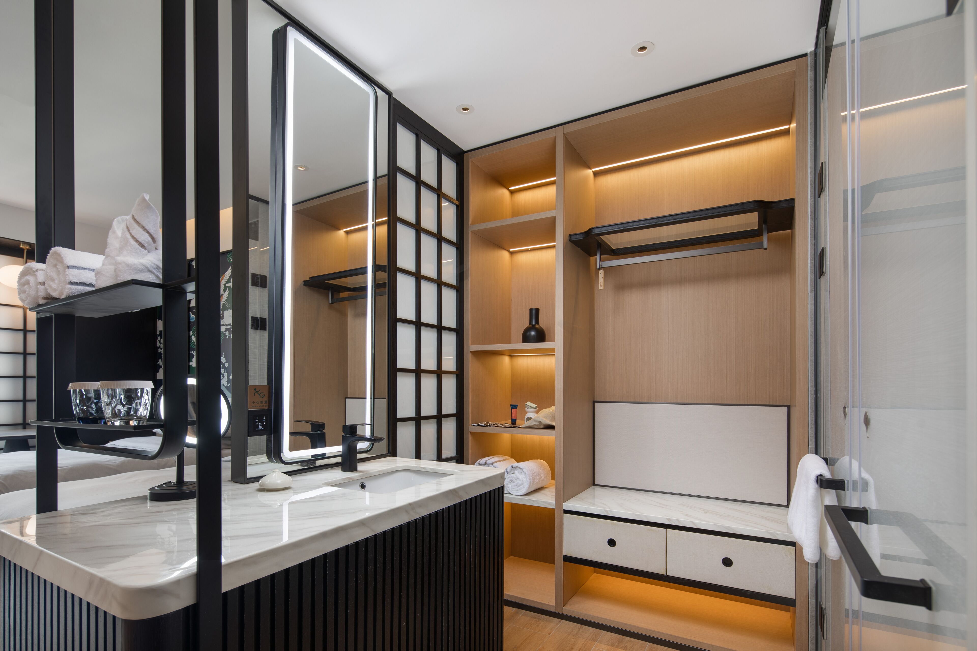 A modern bathroom with a large mirror, a vanity with a sink, and a walk-in closet with shelves and a hanging rack.