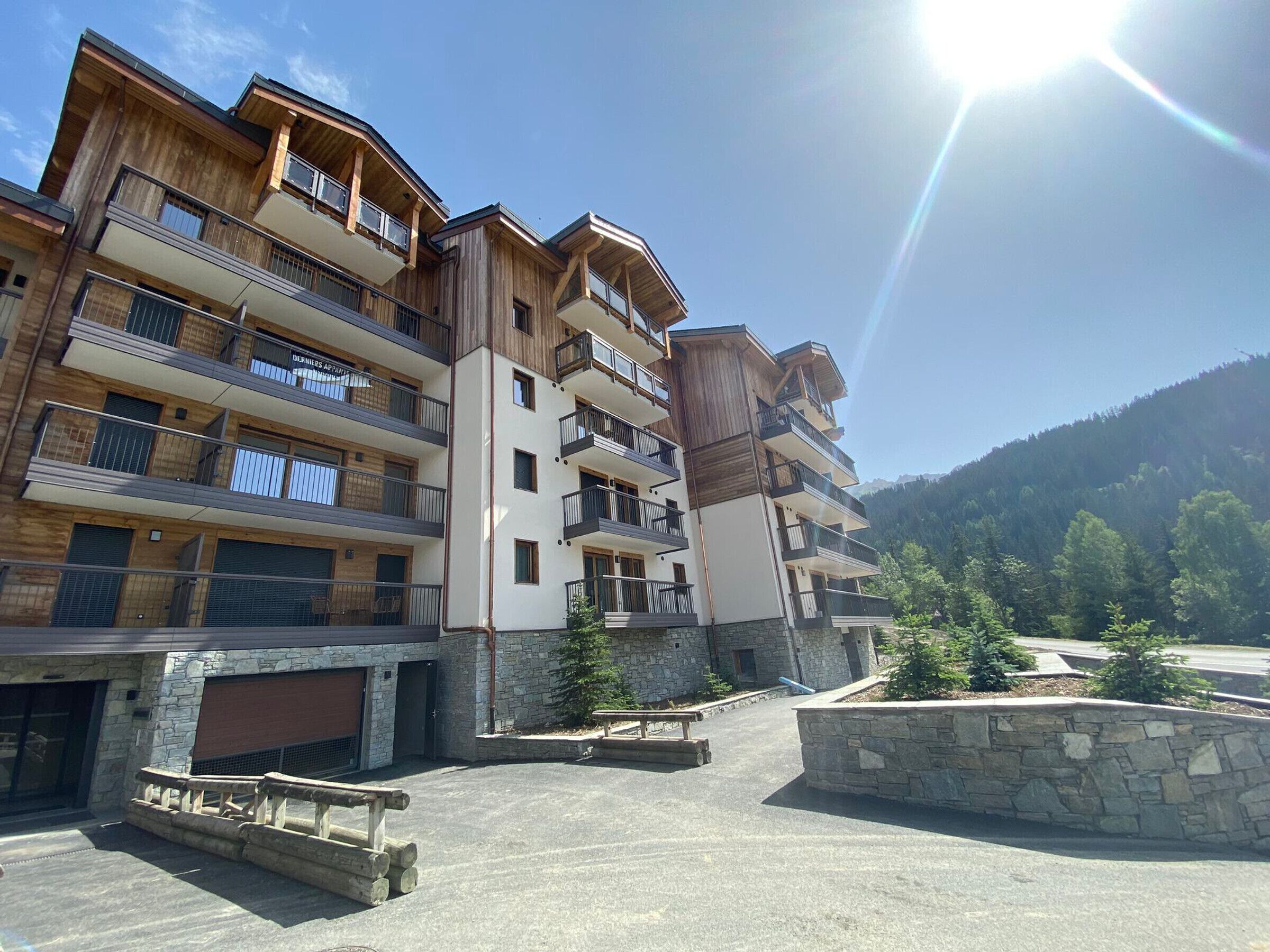 A multi-story hotel with balconies, stone facade, and a parking area with a picnic table.