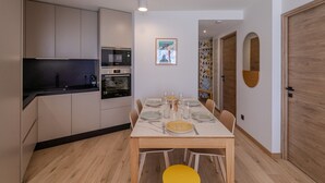 A modern kitchen with built-in appliances, a dining area with a wooden table and yellow chairs, and a wooden door. - Modern 2-room apartment, near slopes, Courchevel (Courchevel 1650)