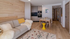 A modern living room with a sofa, a coffee table, and a rug. There is a kitchen area with cabinets and appliances in the background. - Modern 2-room apartment, near slopes, Courchevel (Courchevel 1650)