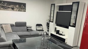 A modern living room with a grey sofa, a glass-top dining table, and a flat-screen TV mounted on the wall. - French apartment for sale in Aulnay sous bois (Aulnay-sous-Bois)