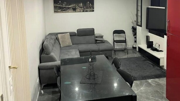 A modern living room with a sectional sofa, a glass-top dining table, and a flat-screen TV mounted on the wall. - French apartment for sale in Aulnay sous bois (Aulnay-sous-Bois)