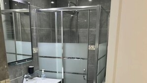 A modern bathroom with a glass shower enclosure, a white sink, and a dark vanity. - French apartment for sale in Aulnay sous bois (Aulnay-sous-Bois)
