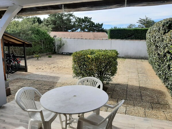 A patio with a round table and two chairs, surrounded by a gravel area and a hedge.