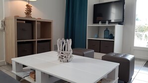 Ett modernt vardagsrum med ett vitt bord, en soffa, en tv på väggen och ett träskåp.