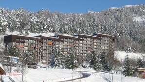 Een hotel met meerdere verdiepingen, met een modern architectonisch ontwerp, omringd door met sneeuw bedekte bomen en een bergachtige achtergrond.