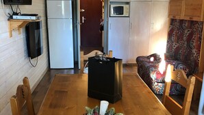 Een gezellige woonkamer met een houten eettafel, een aan de muur bevestigde televisie, een koelkast, een magnetron en een gestreept sofa.