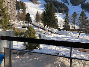 Schneebedeckte Landschaft mit Skipiste, Bäumen und einem Gebäude mit außergewöhnlicher Architektur.