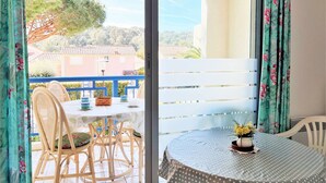 Un balcon doté de chaises et d’une table en osier, offrant une vue sur un quartier résidentiel avec ses maisons et ses arbres.