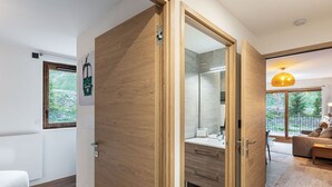 A modern bathroom with a wooden door, a large mirror, and a vanity.