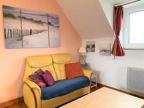 Um sofá amarelo com almofadas coloridas, uma mesa de madeira e um quadro com tema praiano na parede.