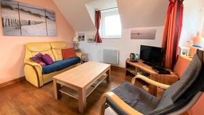 Una sala de estar acogedora con un sofá amarillo, un sofá azul, una mesa de centro de madera, un televisor y una estantería.
