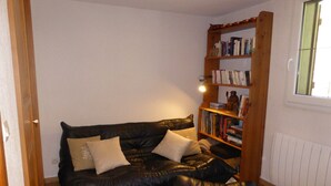 Un soggiorno con un divano in pelle nera, una libreria in legno piena di libri e una finestra con persiane.