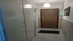 Un couloir se terminant par une porte en bois, un luminaire blanc au plafond et un tapis noir sur le sol.