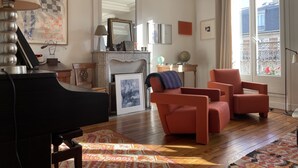 Un salon avec une cheminée, un piano et deux fauteuils rouges.