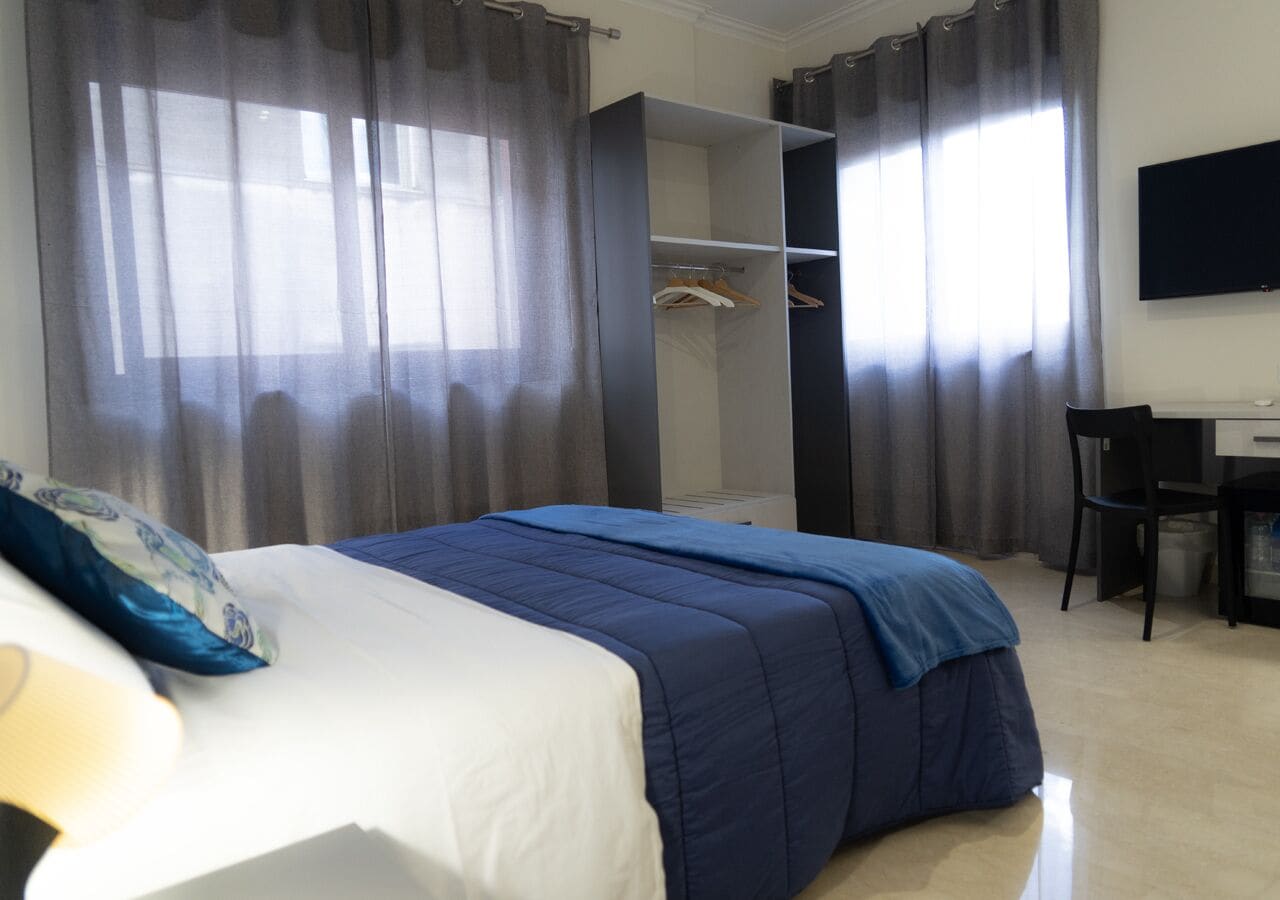 A bedroom with a bed, a desk, and a wardrobe.