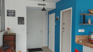 Ein Flur mit einem Holzstuhl, einem Schreibtisch und einem roten Hocker. Es gibt zwei Türen, eine führt in einen Raum, die andere in einen Flur.