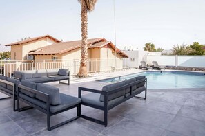 A poolside area with a modern pool, a palm tree, and a building with a tiled roof.