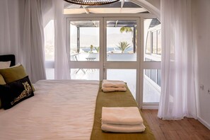 A bedroom with a bed, a bench, and a view of the outside.