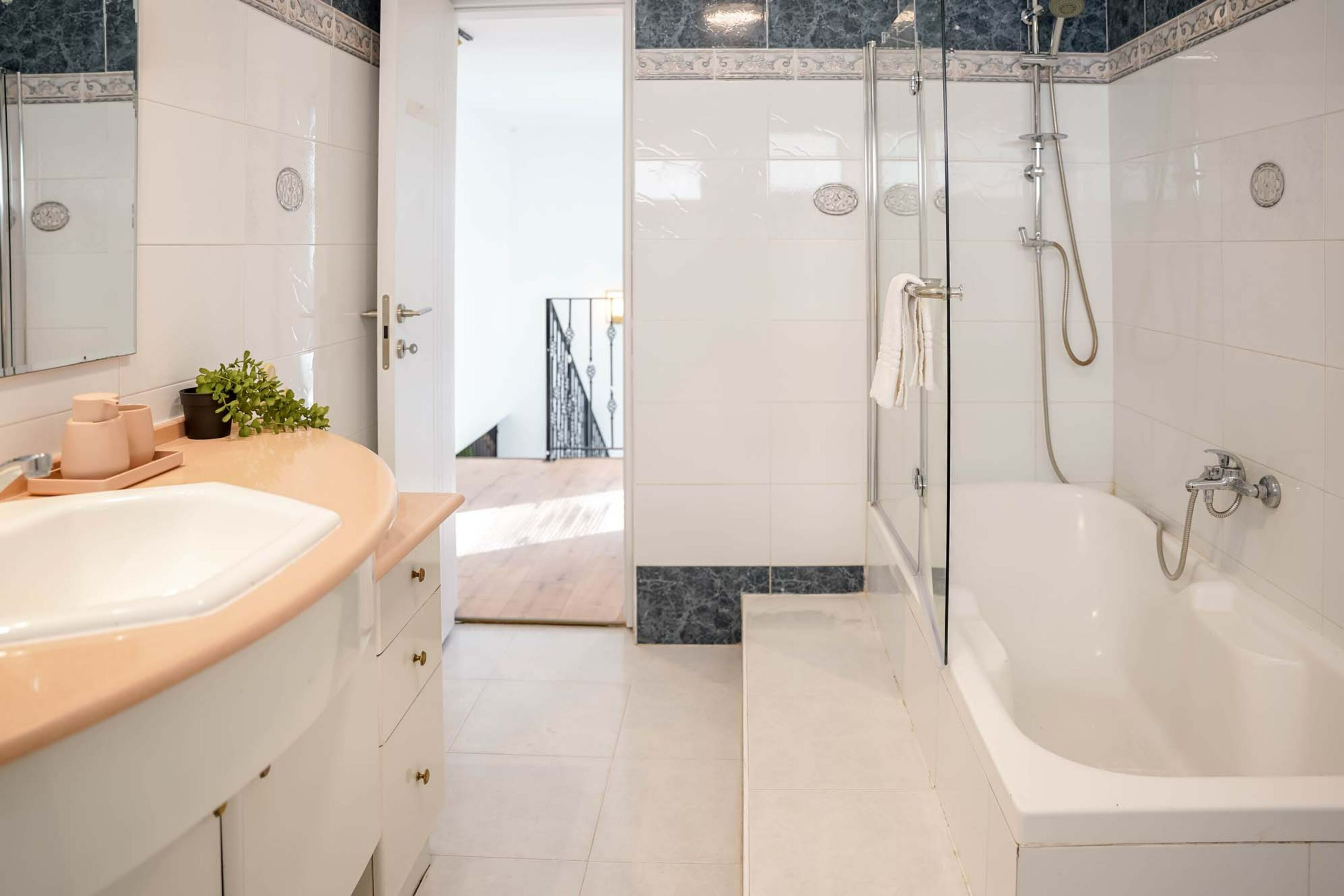 A modern bathroom with a large white bathtub, a glass-enclosed shower, and a vanity with a beige countertop.