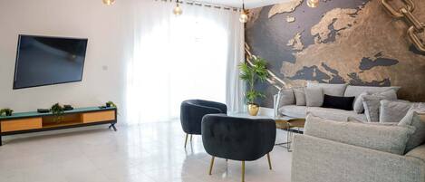 A modern living room with a flat-screen TV, a sofa, two armchairs, a coffee table, and a decorative wall with a map.