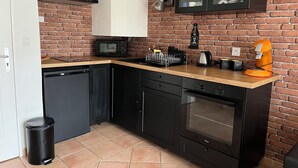 A compact kitchen with a brick wall, black cabinetry, a microwave, a coffee maker, and a toaster. - Charming, quiet duplex cottage with terrace/garden (Ardon)