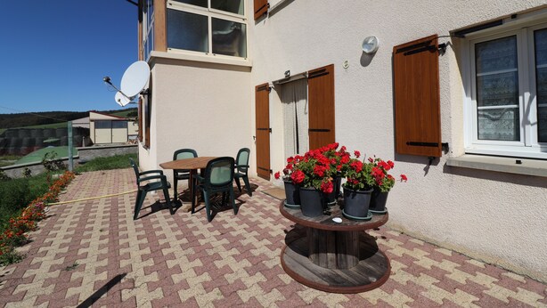 Een terras met een ronde tafel en stoelen, plantenpotten en een schotelantenne.