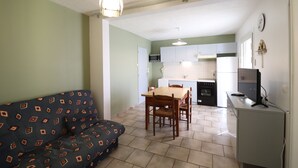 Een compacte woonruimte met een bank, eettafel, stoelen, een televisie en een kitchenette.