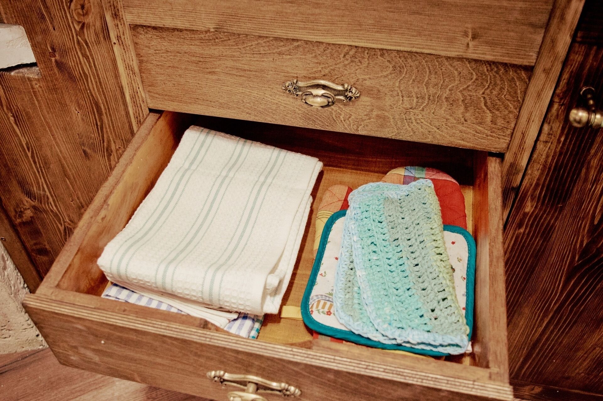 A wooden chest with a brass handle, containing a folded white towel and a crocheted item with a blue border.