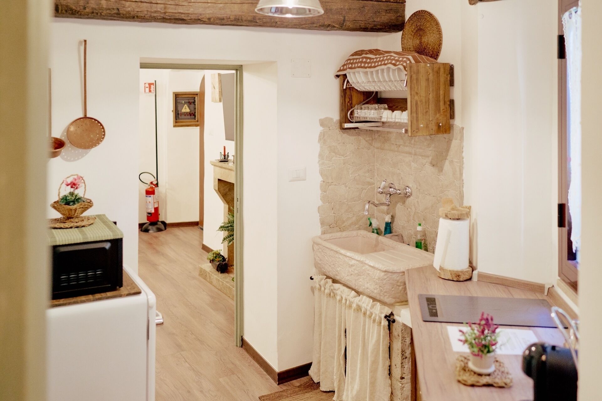 Eine Küche mit Spüle aus Stein, Holzschränken und einer kleinen Arbeitsplatte. Ein Feuerlöscher und ein Korb mit Blumen stehen auf der Arbeitsfläche.