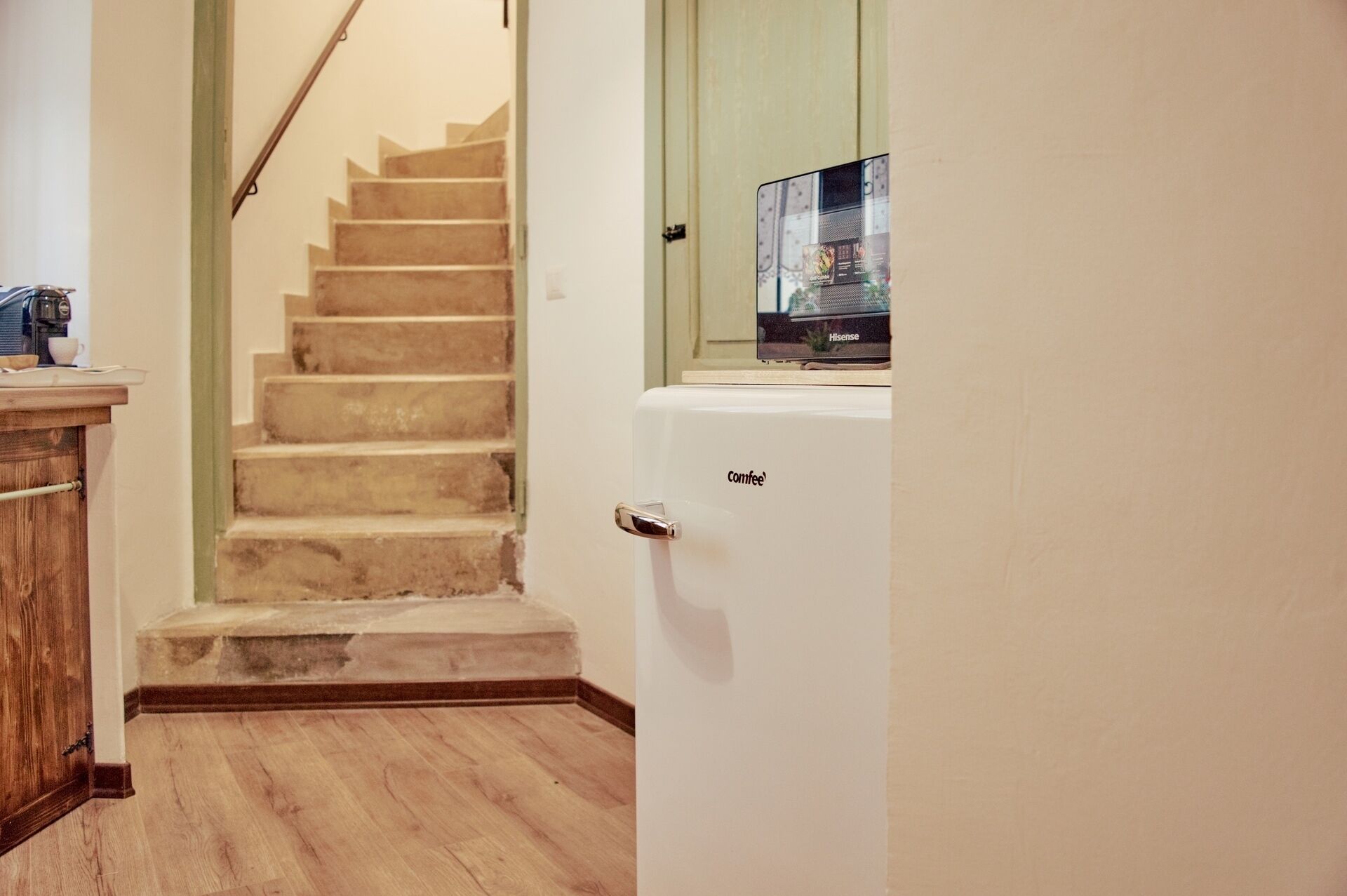 A staircase leading to a second floor, a wooden cabinet, and a white refrigerator with the brand 'Comfee' on it.