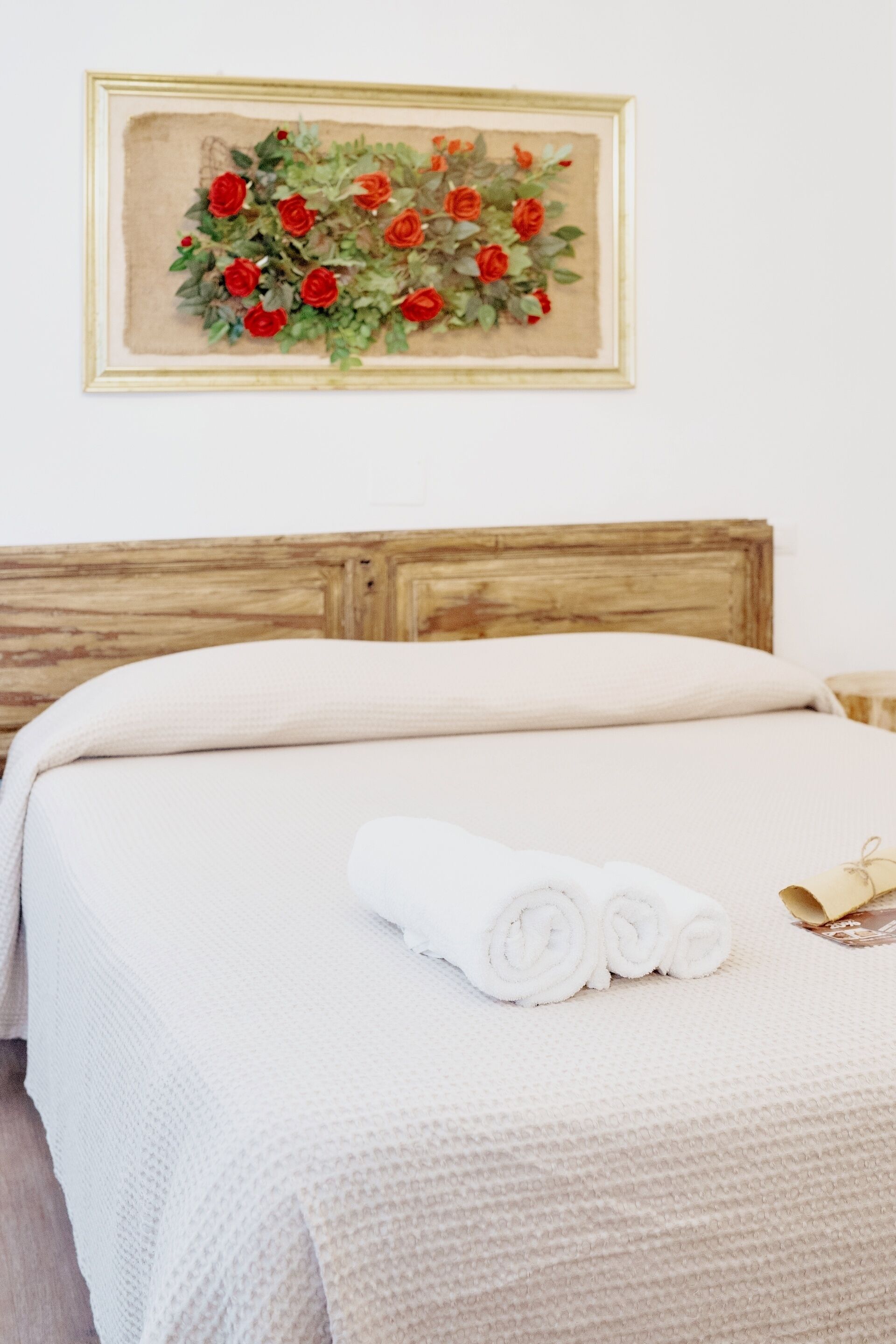 Un lit bien fait, avec du linge de lit blanc et des serviettes pliées, une tête de lit en bois et une œuvre d’art florale encadrée accrochée au mur.