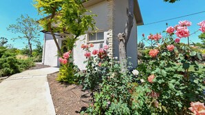 A house with a stone facade, a small window, and a garden with pink roses. - YalaRent Valley view complex In Merhavia with Private heated Pool (Emek Izrael)