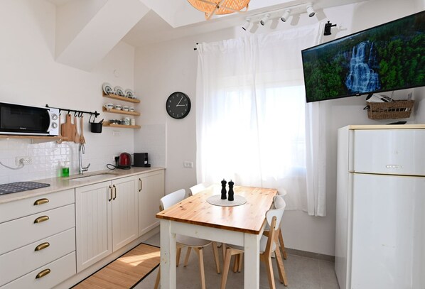 A modern kitchen with white cabinets, a wooden table, and a flat-screen TV mounted above the counter.