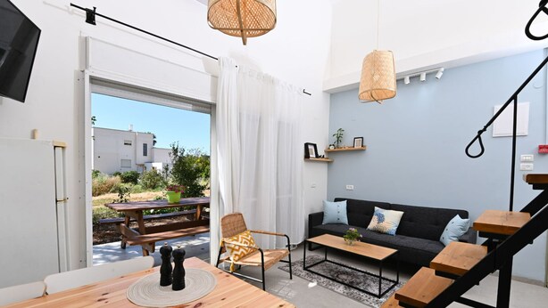 A modern living space with a wooden dining table, a black sofa, and a staircase. - YalaRent Valley view complex In Merhavia with Private heated Pool (Emek Izrael)