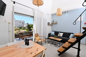 A modern living space with a wooden dining table, a black sofa, and a staircase.