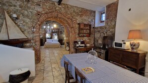 Une pièce chaleureuse avec une arche en pierre, une table à manger recouverte d’une nappe à carreaux, un buffet en bois, un four à micro-ondes et une petite maquette de voilier.