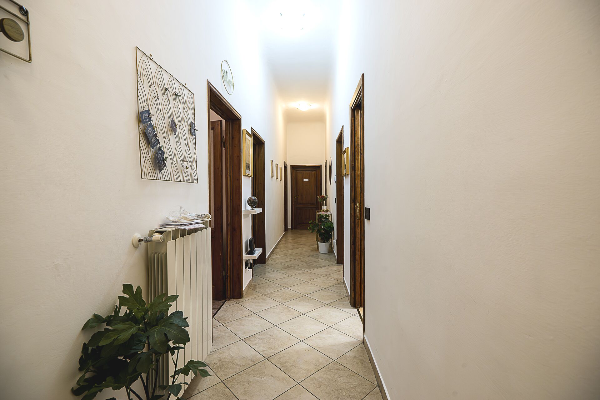 A narrow hallway with tiled flooring, a radiator, and a potted plant.