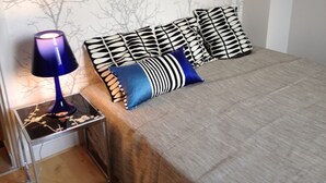 A bed with a grey bedspread, a blue and white striped pillow, and black and white patterned pillows. - Magnificent view, hyper center apartment (Tours)