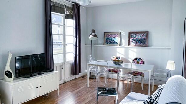 A modern living room with a TV, white cabinets, a dining area with chairs, and artwork on the wall. - Magnificent view, hyper center apartment (Tours)