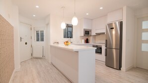 Uma cozinha moderna com ilha central, eletrodomésticos de aço inoxidável, iluminação pendente e vista para a sala de estar.
