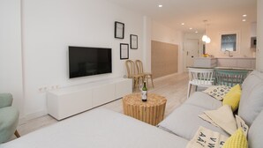 Uma sala de estar moderna com uma TV de tela plana, uma mesa de centro redonda de madeira e um sofá com almofadas.
